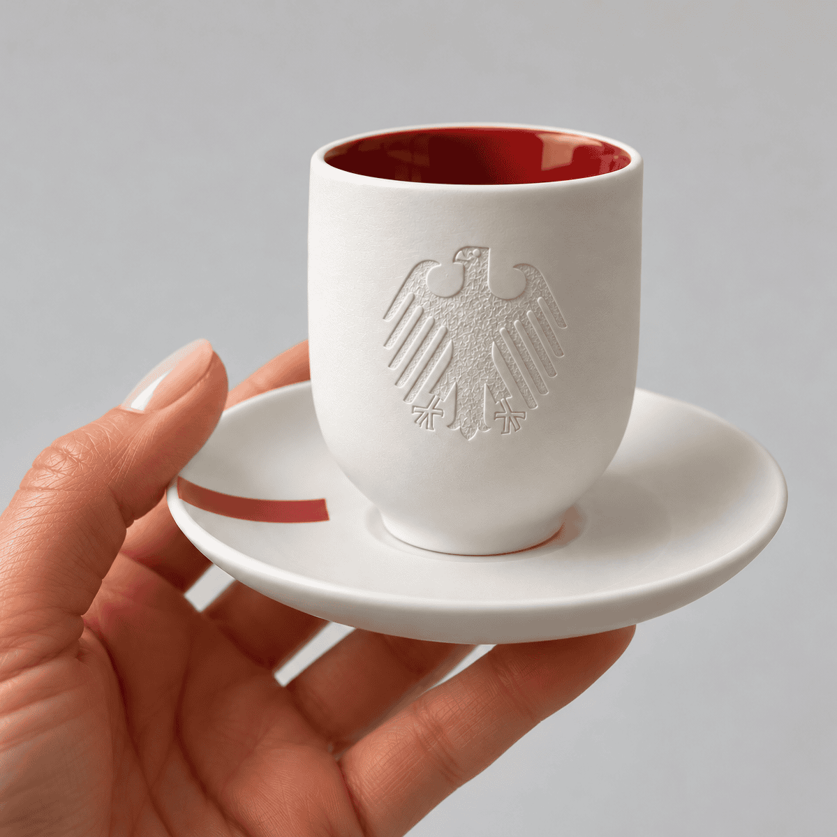 ndividuell gestaltete Espressotasse aus weißem Porzellan mit haptischem Bundesadler, roter Innenglasur und passendem Unterteller mit rotem Dekor.